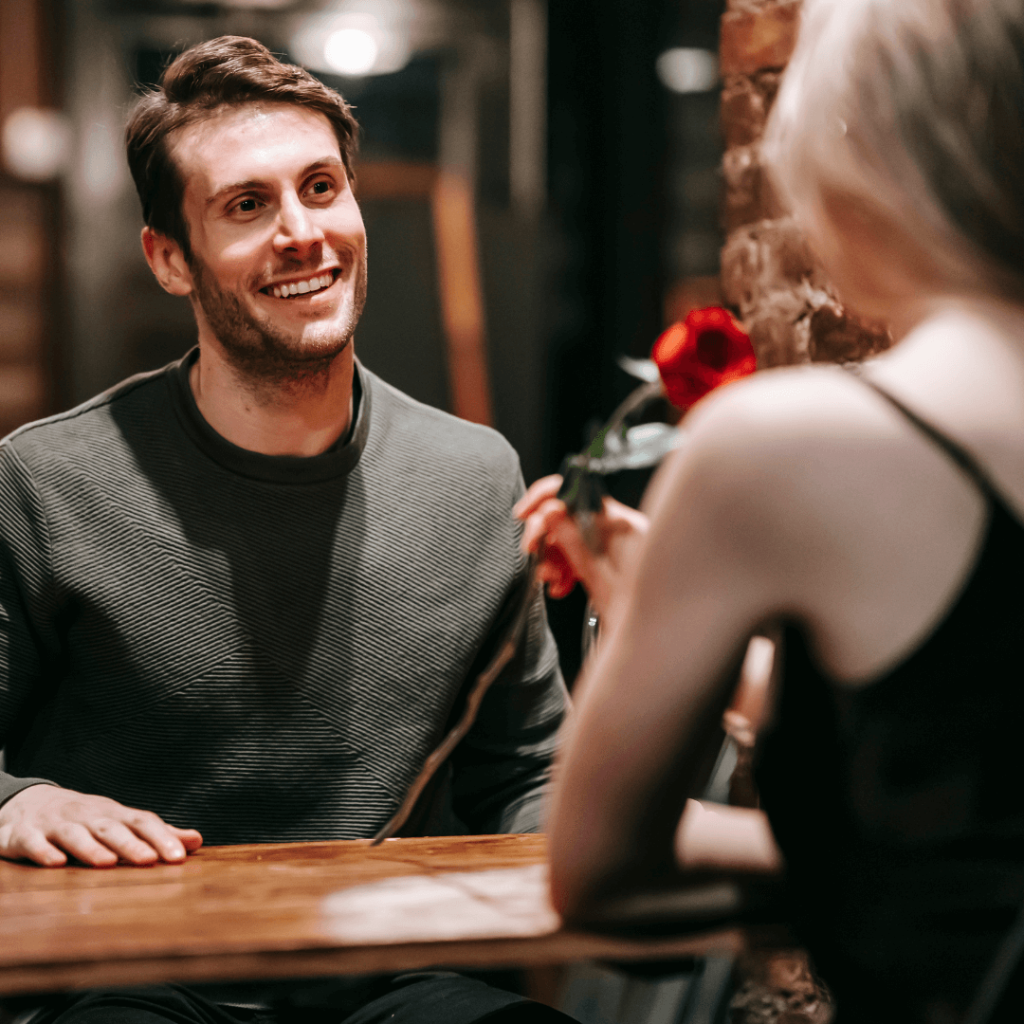 A man holding a rose, smiling at a woman during a date at a cozy restaurant. The setting captures the excitement of dating and the importance of professional guidance. This photo highlights the services of a one-on-one dating coach in Orlando.