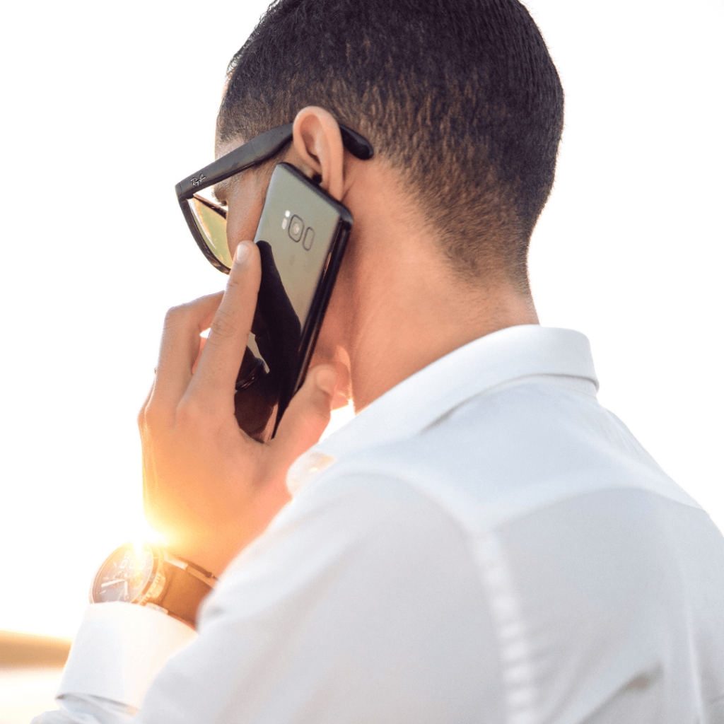 A close-up of a man in sunglasses and a white shirt speaking on his smartphone during a consultation. The image highlights the convenience and accessibility of phone consultations offered by Orlando Date Coach.