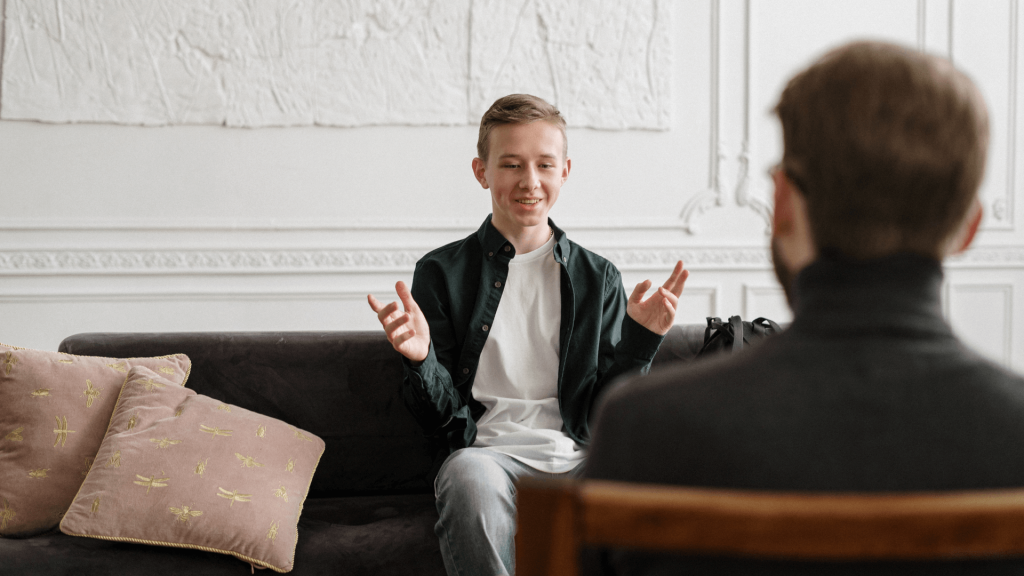 A young man sitting on a sofa, engaging in a lively conversation with a dating coach.