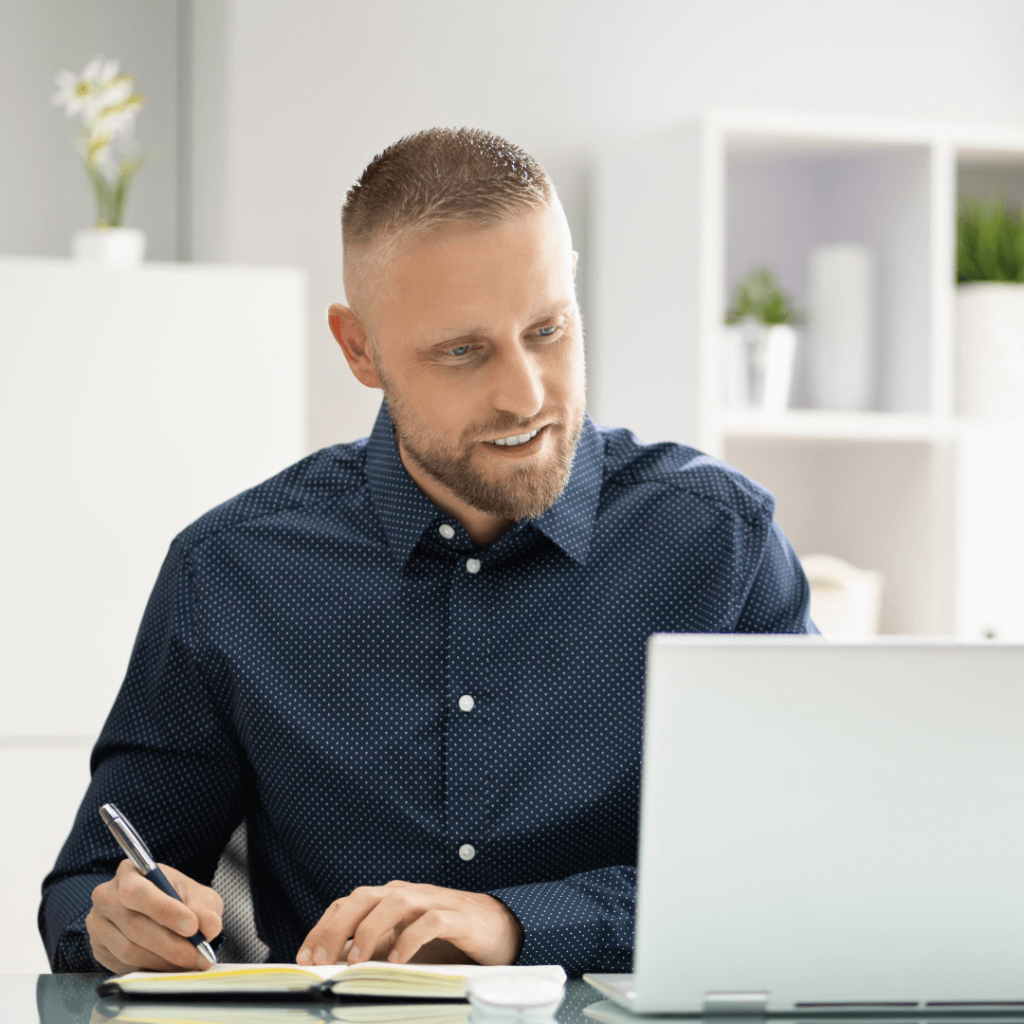 A man in a blue shirt taking notes while engaged in a virtual one-on-one coaching session on his laptop. The image represents the personalized online coaching services offered by Orlando Date Coach.